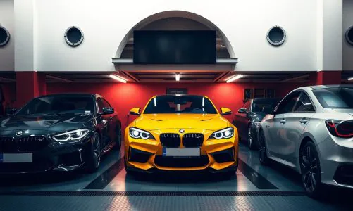 Three high-end sports cars parked in a well-lit modern garage, with a bright yellow BMW centered between a black and a silver car.
